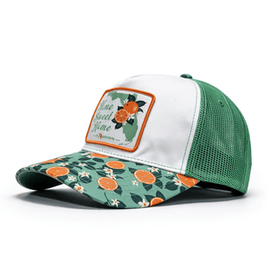 Trucker hat with floral and orange design on the visor with a white crown and a patch that says 