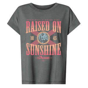 Dark gray womens tee with a Florida flag in the center and text 'RAISED ON SUNSHINE'.