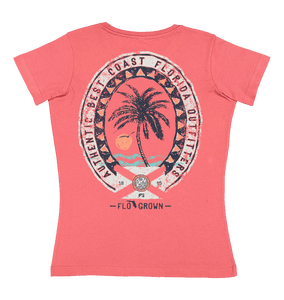 Pink tee with a vintage style graphic of a palm tree on the beach at sunset and an oval crest around it.