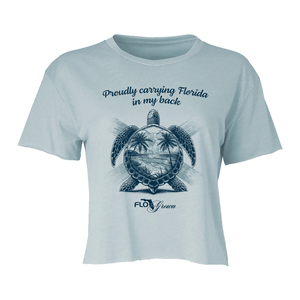 Light blue crop top with turtle graphic with palm trees and the Florida flag and text 'Proudly carrying Florida in my back'.