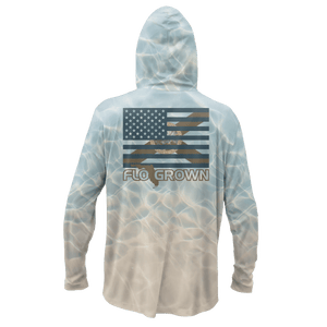 A hooded long-sleeve shirt shown from the back on a white background. The garment has a light blue and beige water-ripple print, featuring a distressed American flag graphic with the text 'FLO GROWN' across the upper back.